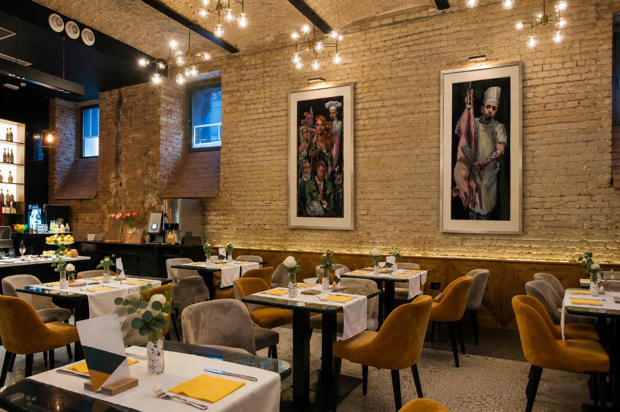 Two framed paintings on the exposed brick wall of a café dining room.